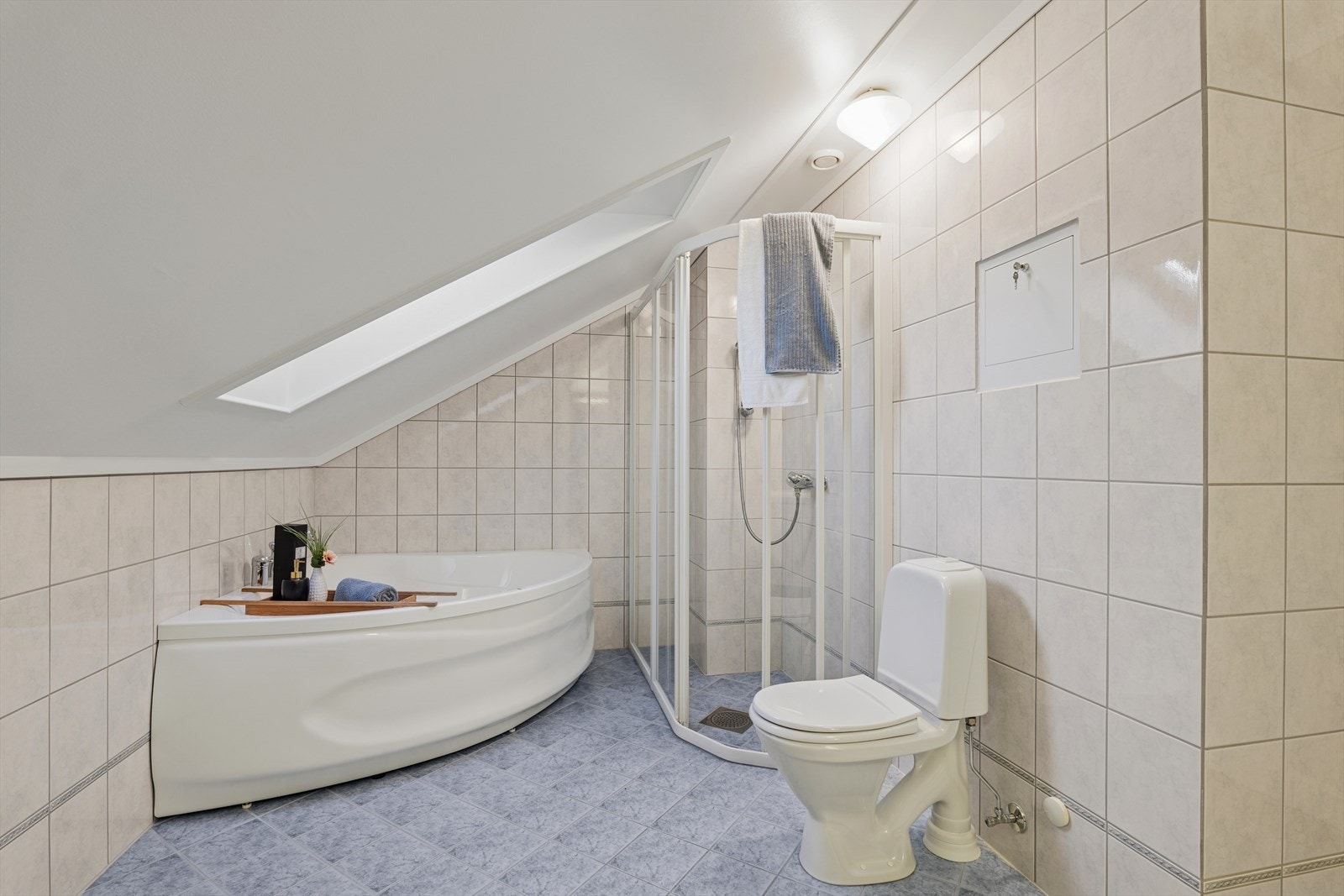 Badet i loftsetasjen er utstyrt med dusjkabinett, hjørnebadekar og toalett. Skråtak med takvindu gir naturlig lys og en luftig følelse Galleribilde