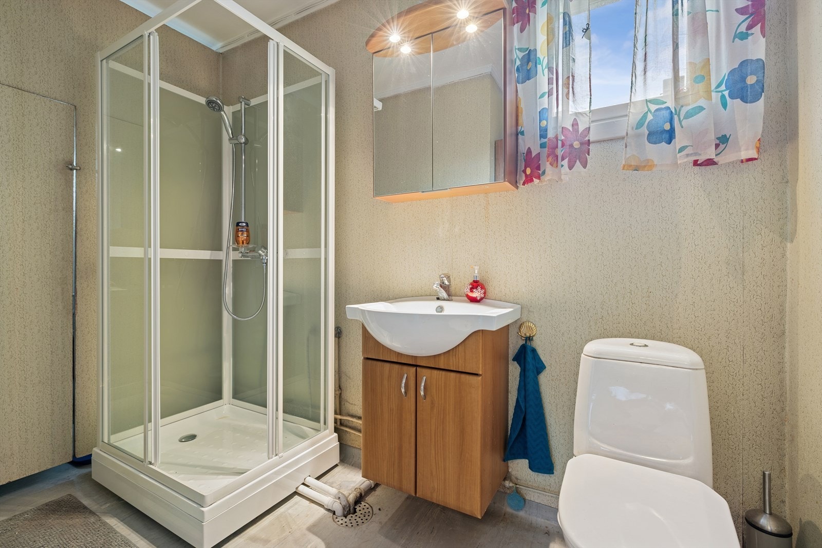 Badet har en enkel innredning med gulvmontert toalett, dusjkabinett, servantseksjon og opplegg for vaskemaskin. Galleribilde