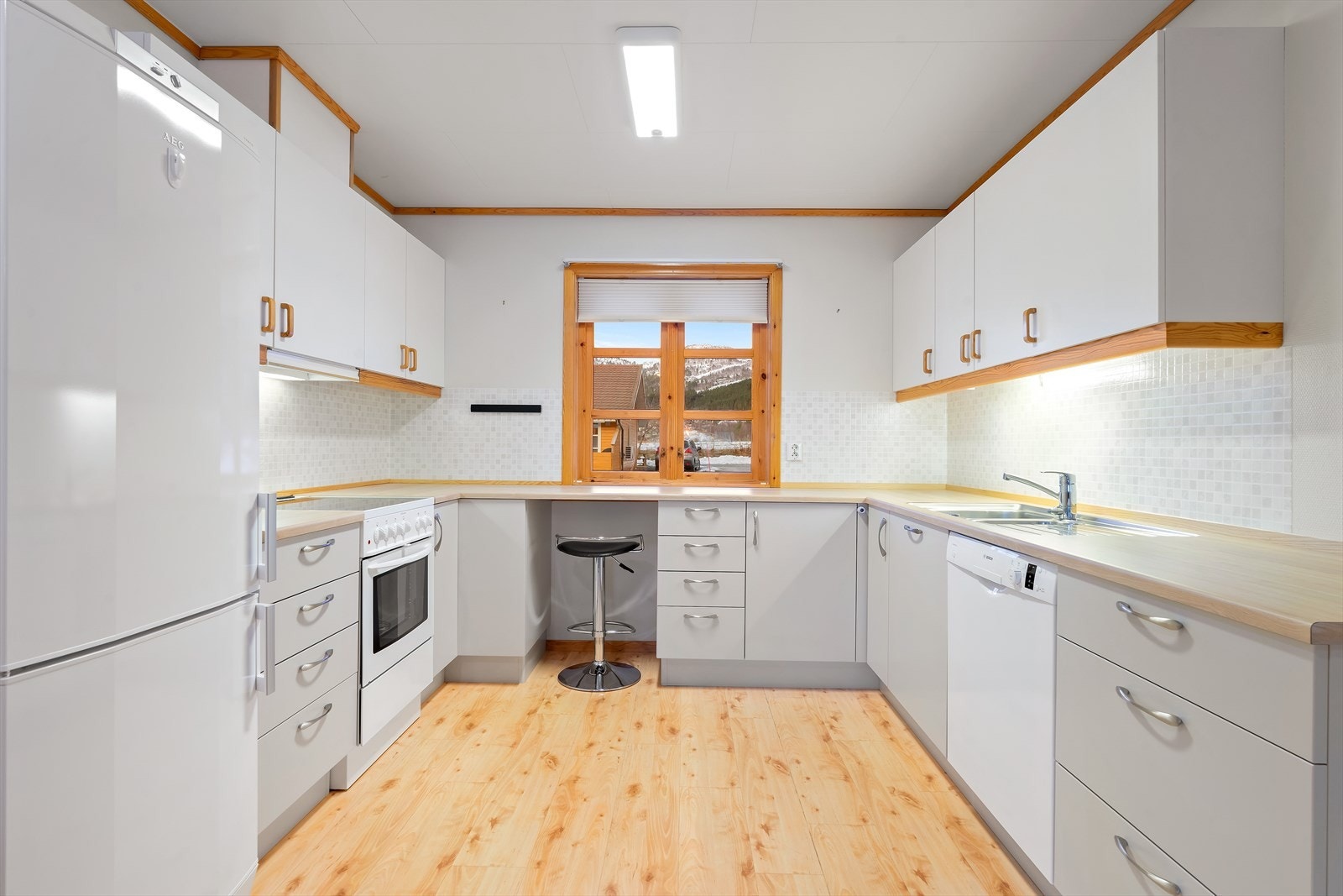 Effektiv u-formet kjøkkenløsning med integrert oppvaskmaskin og en liten spiseplass under kjøkkenvinduet. Galleribilde