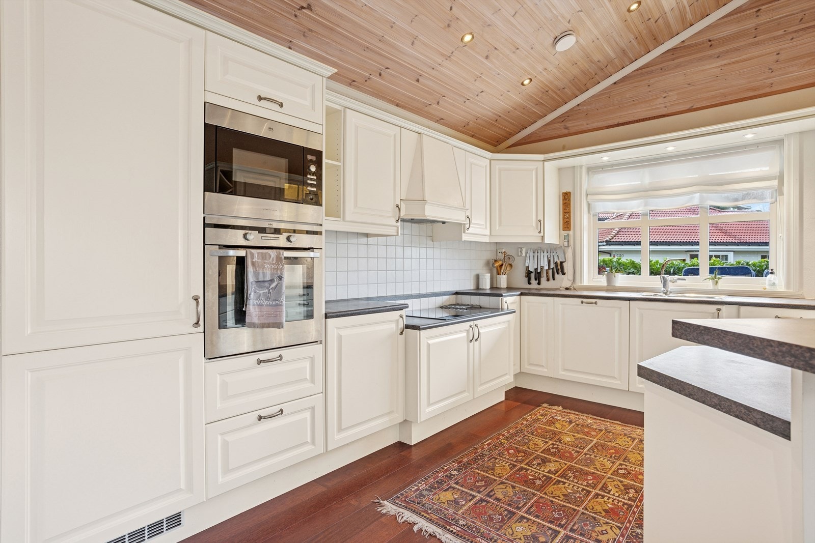 Kjøkkenet har profilerte hvite fronter og laminert benkeplate, med delvis flislagt vegg over benk. Galleribilde