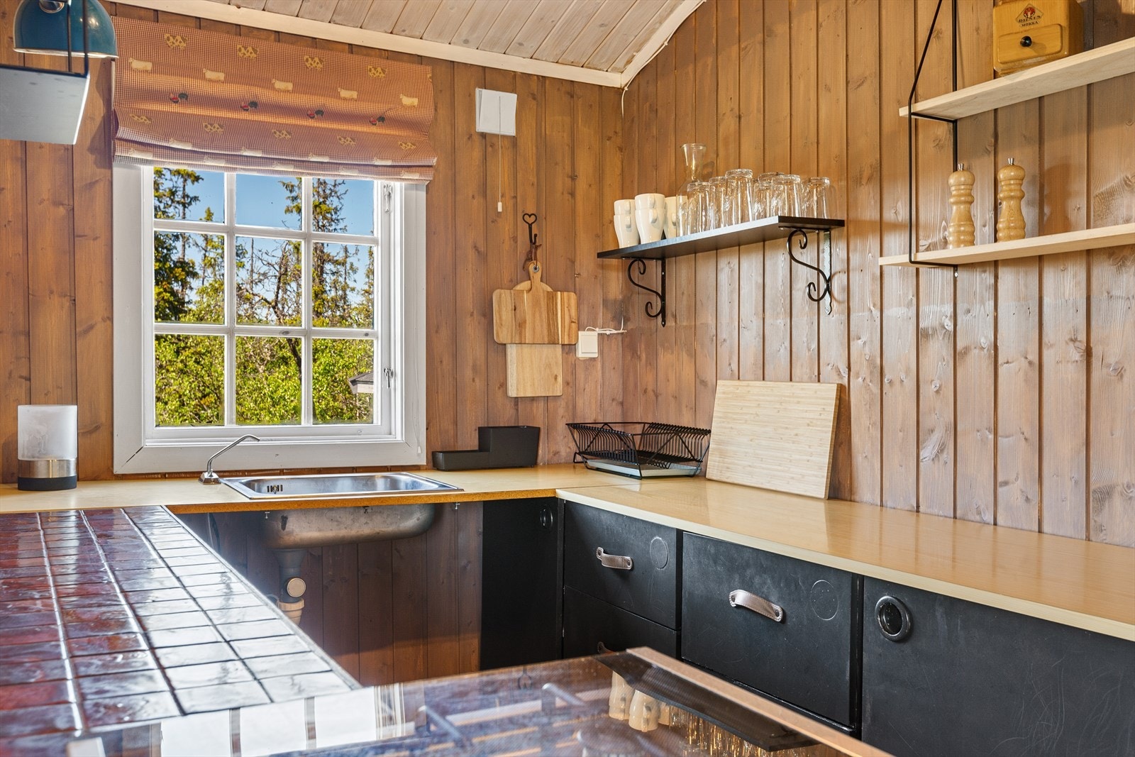 Kjøkkenet har også en smal, flislagt benk, og over kjøkkenbenkene er det mange åpne hyller. Frittstående gasskomfyr og kjøl- og fryseskap på solcelle. Galleribilde