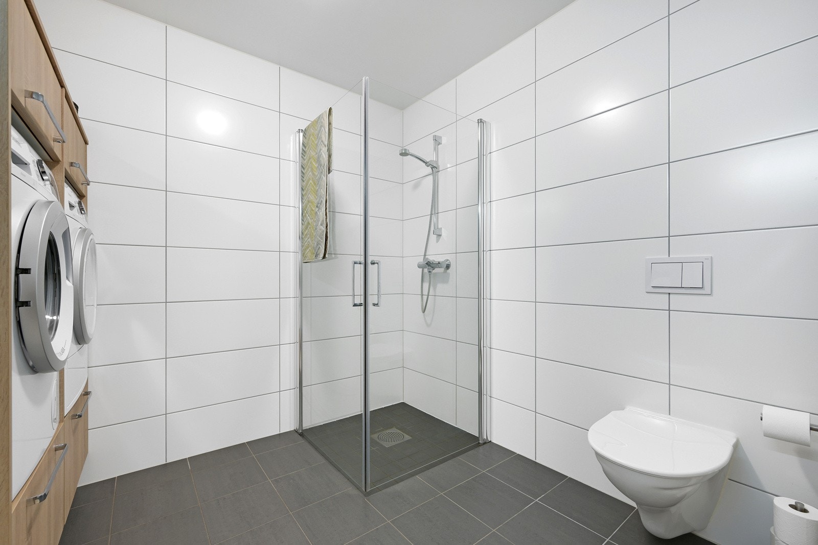 Badet er innredet med servant, speil med lys, veggmontert wc og dusjhjørne Galleribilde