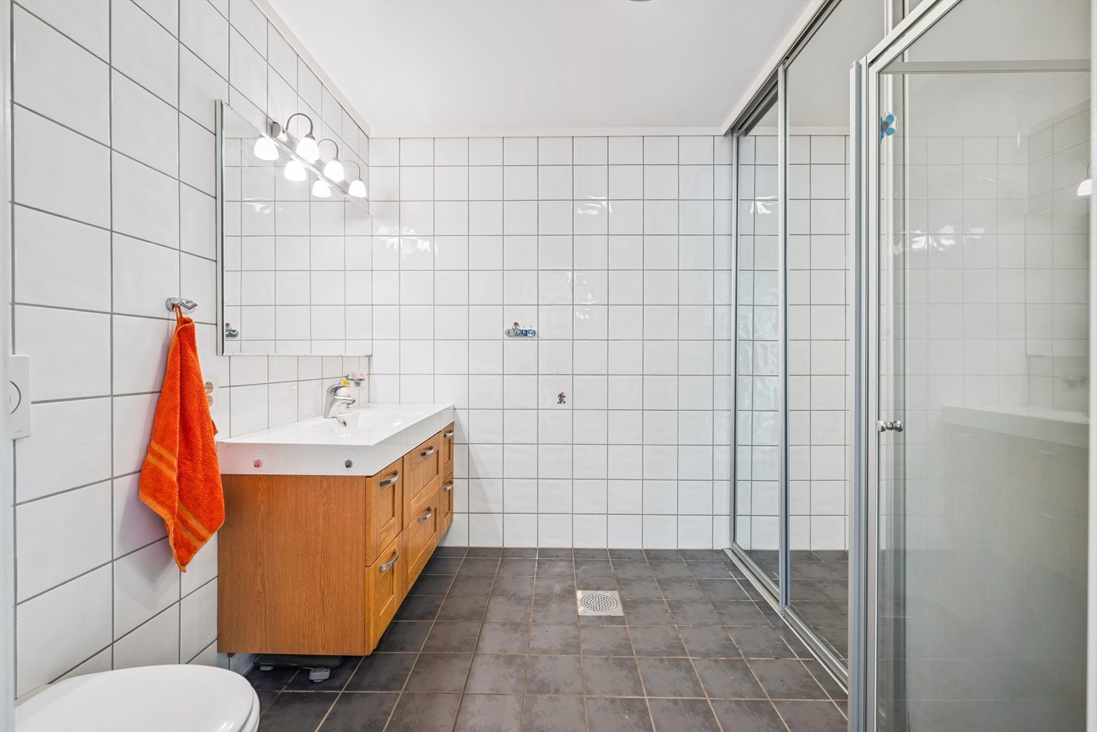 Flislagt bad med skyvedørsgarderobe med speildører, helstøpt servant i baderomsinnredning, vegghengt toalett og dusjkabinett. Galleribilde