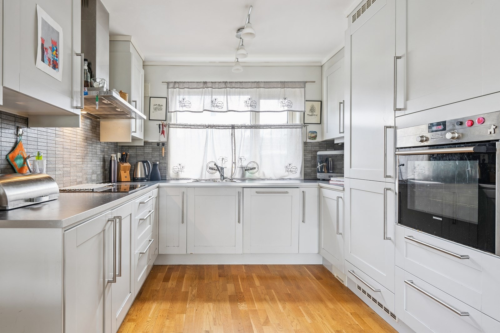 Lys kjøkkeninnredning med profilerte fronter og laminerte benkeplater. Integrerte hvitevarer. Galleribilde