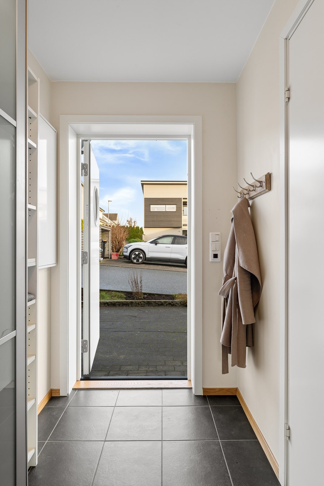 En pen fliselagt entré/gang med varmekabler i gulv og plass til å henge fra seg både yttertøy og sko. Galleribilde