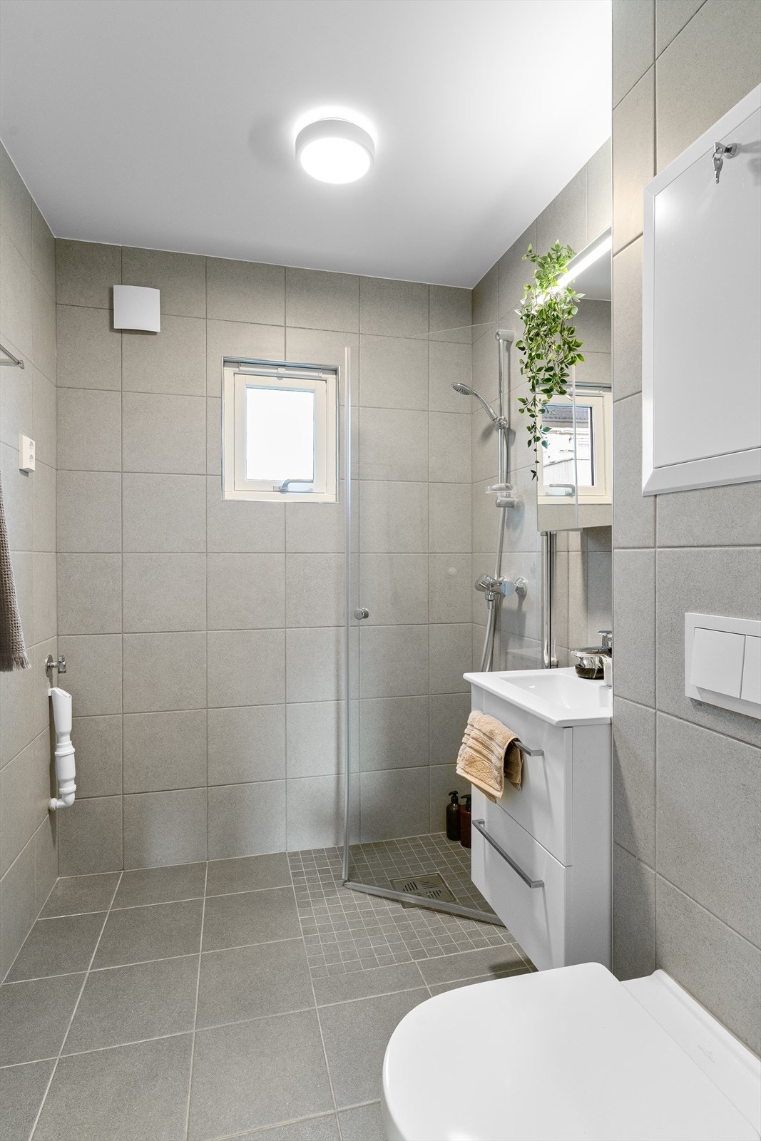 Badet har hvit innredning med nedfelt servant, speilskap, veggmontert toalett, dusjvegger/hjørne og opplegg for vaskemaskin. Galleribilde