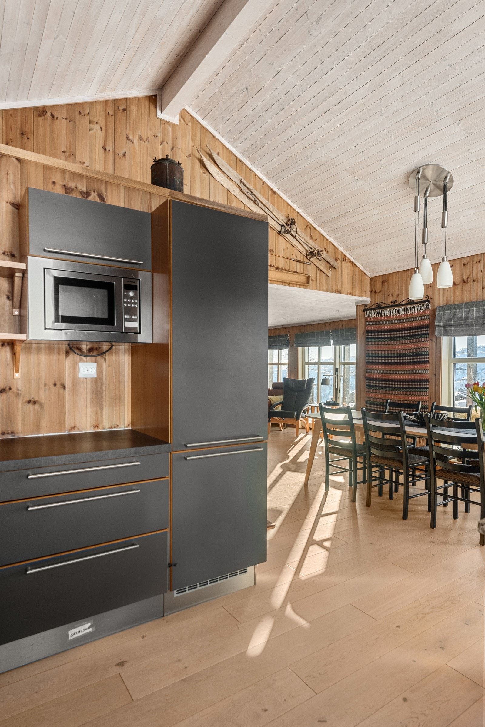 Kjøkken med enstavs parkett med varmekabler på gulv og panel på vegger. Ekstra takhøyde og vindu i gavl. Galleribilde