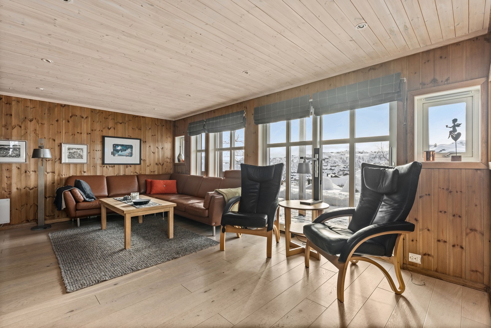 Romslig stue med enstavs parkett med varmekabler på gulv, panel på vegger og spotter i tak. Galleribilde