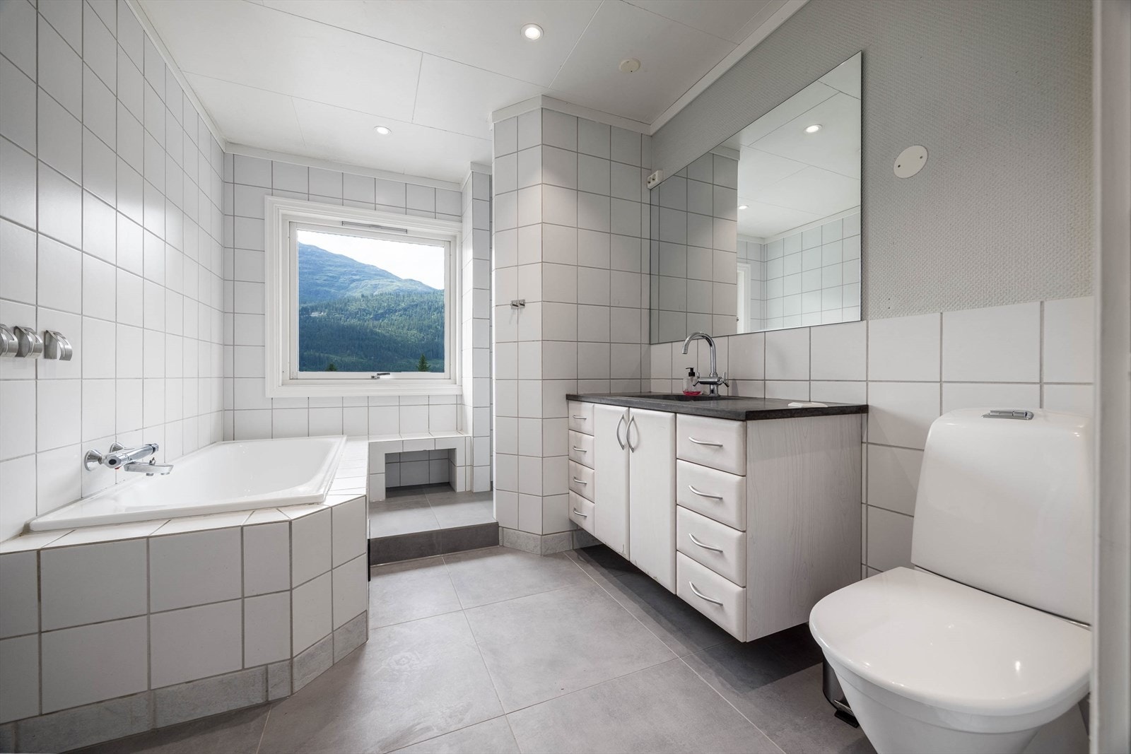 Lyst og delikat baderom med badekar og dusjnisje. Galleribilde