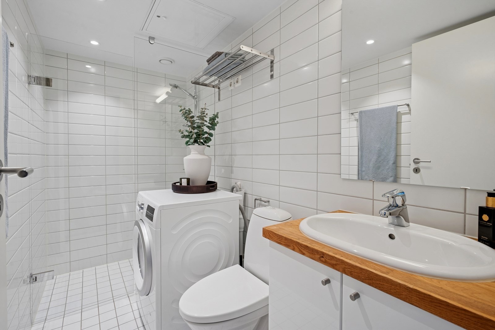 Delikat og tidløst bad innredet med toalett, dusjhjørne, servant nedfelt i eik benkeplate og speil med overlys. Galleribilde