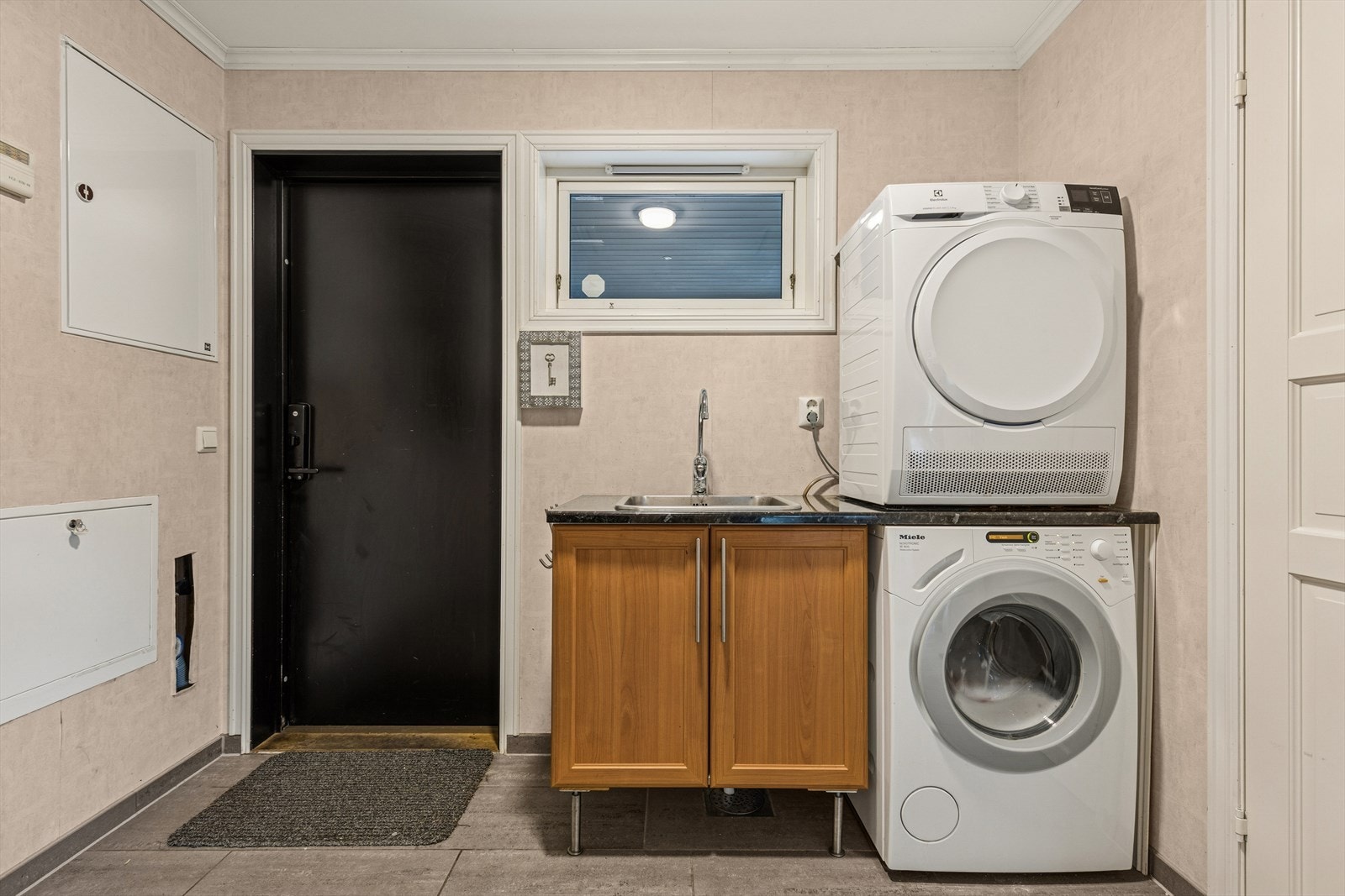 Vaskerom med fliser på gulvet, utgang og opplegg til vaskemaskin og tørketrommel. Galleribilde