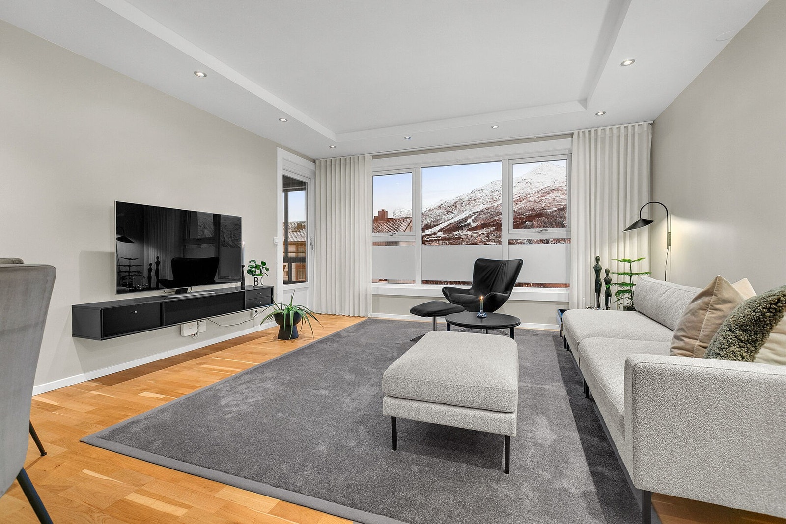 Stue med fin utsikt mot fjellet og byen, store vinduer, led-spotter i tak og parkett på gulv Galleribilde