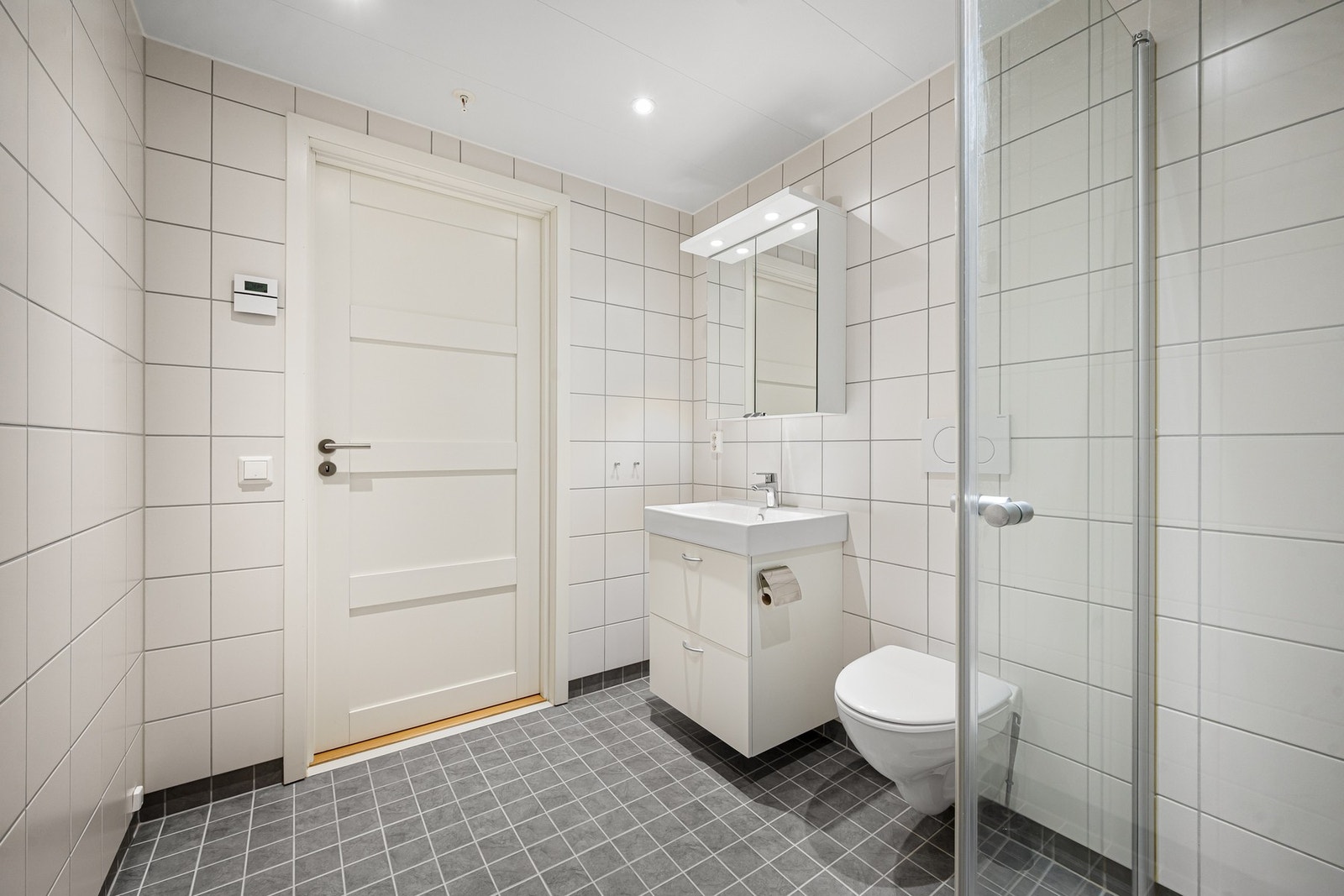 Badet er innredet med dusjkabinett, toalett, samt servant og speil med skap for oppbevaring Galleribilde