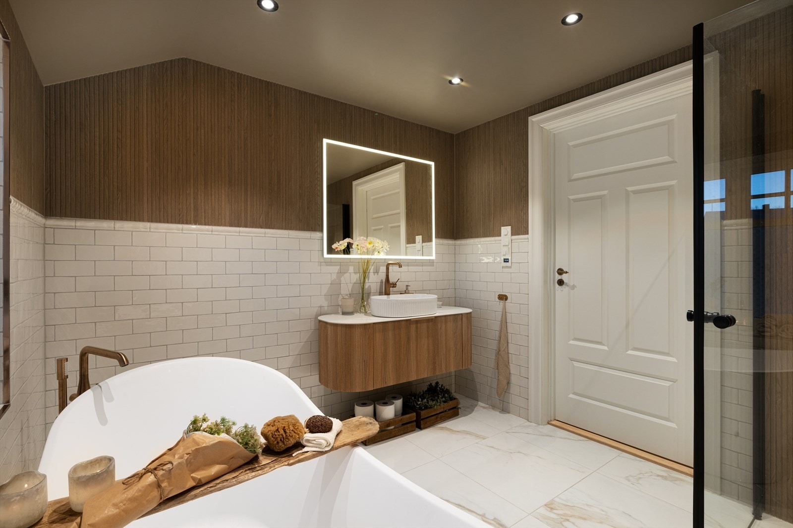 Badet er innredet med sort baderomsmøbel med heldekkende benkeplate og skålservant, speil med integrert belysning, dusjhjørne med glassdører, vegghengt toalett og et deilig badekar. Galleribilde