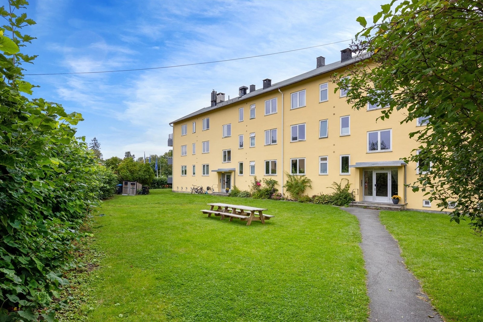 Tomten er fellesareal, og er pent opparbeidet med plenarealer, prydbusker og diverse beplantning, felles sittegrupper og asfalterte internveier. Bilde fra sommeren 2025 Galleribilde