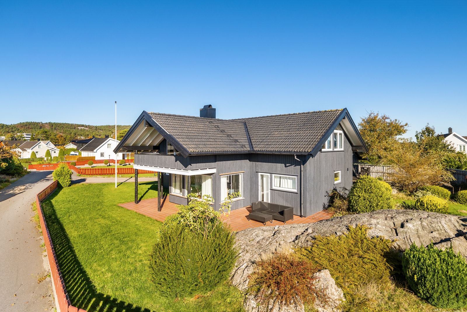 Eneboligen sett fra hagen – plen, terrasse og grå kledning. Galleribilde