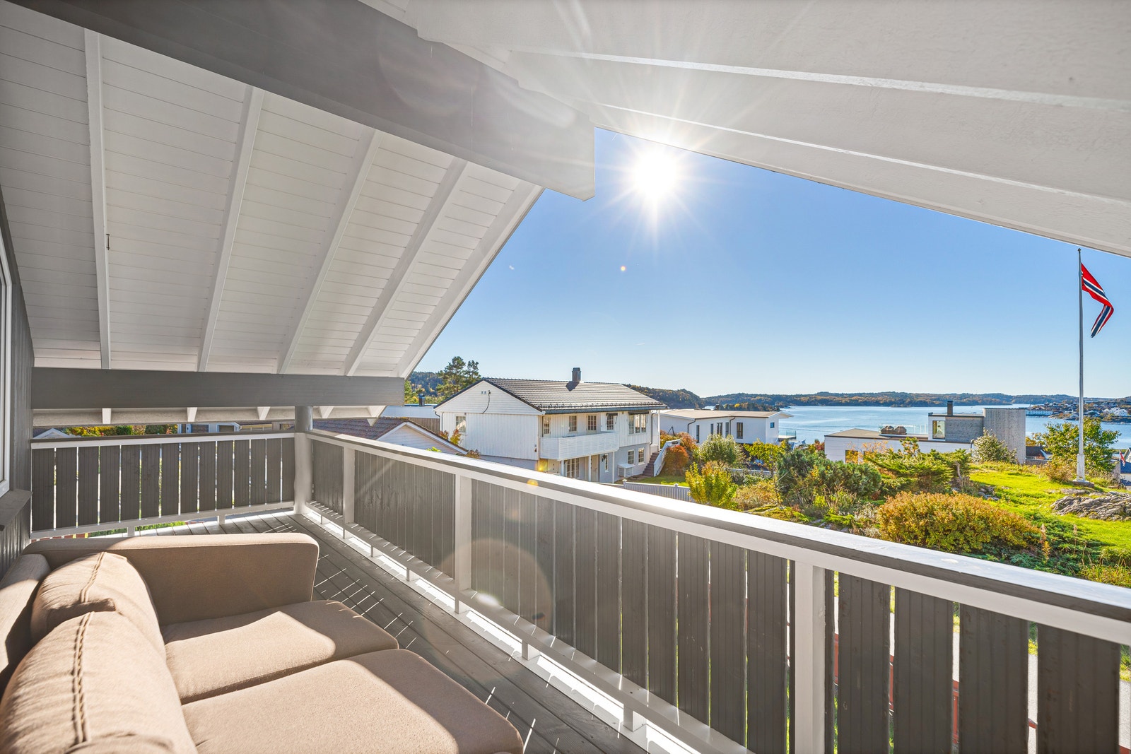 Overbygd terrasse med sittegruppe, sofamøbler og utsikt over nabolag og sjø. Galleribilde