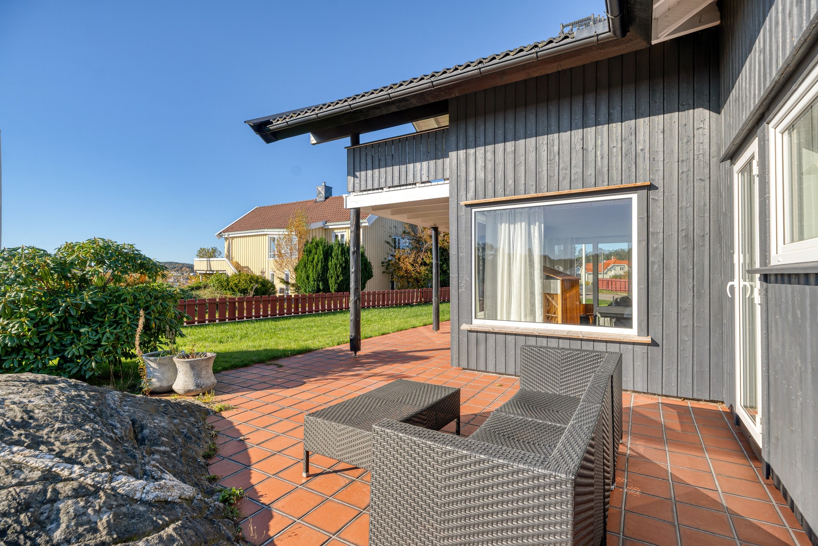 Hage med terrakottafliser og rottingmøbler inntil husveggen. Galleribilde