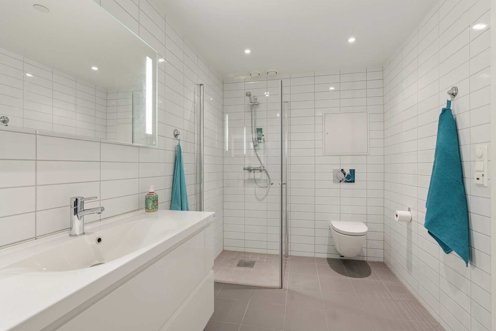 Lyst, flislagt baderom med innredning med nedfelt servant, veggmontert toalett og dusjvegger/hjørne. Galleribilde