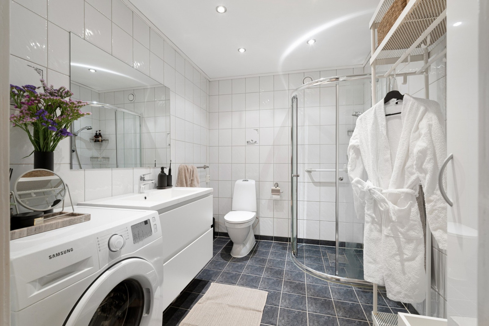 Flislagt bad med dusjhjørne, servantinnredning og praktisk løsning for vaskemaskin. Galleribilde