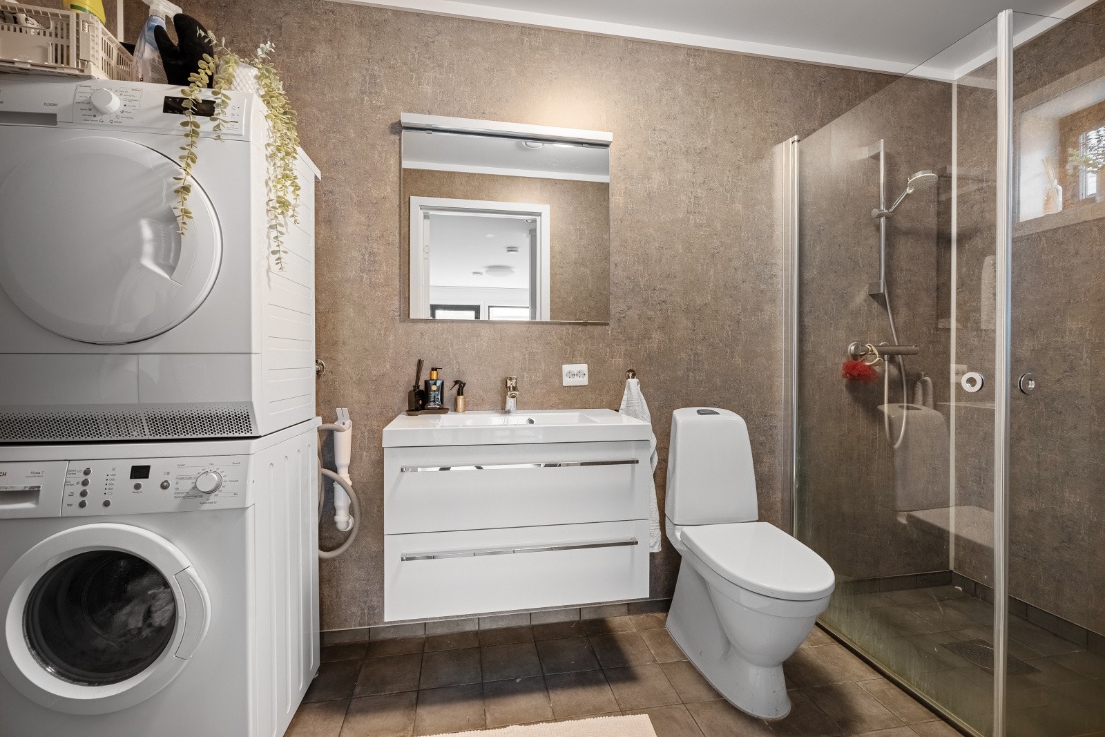 Bad/vaskerom med flislagt gulv med elektriske varmekabler. Innredet med nedfelt servant, toalett og dusjhjørne med innfellbare dører. Opplegg for vaskemaskin Galleribilde