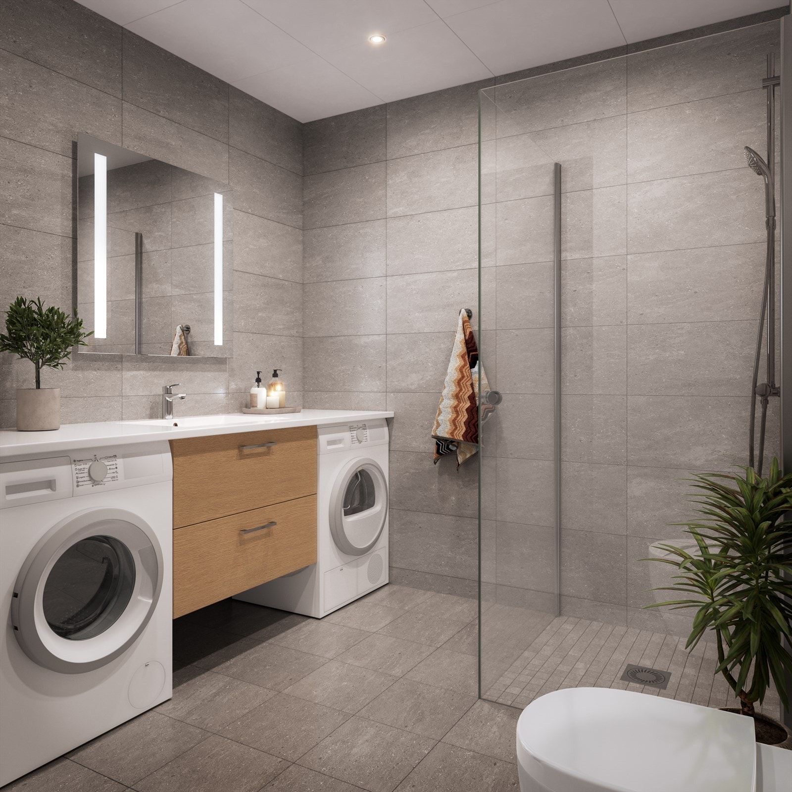 Badet har grå fliser på vegger og gulv. Helstøpt benkeplate med servant. Praktisk plassering av vaskemaskin og tørketrommel under benkeplaten Galleribilde