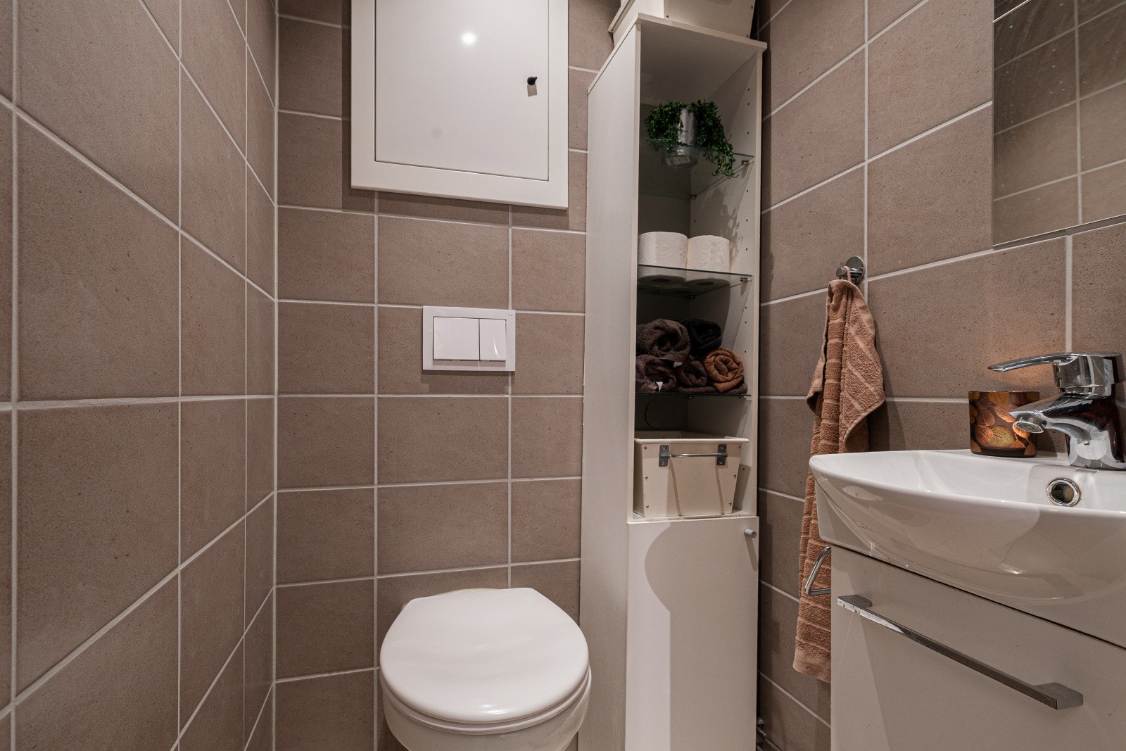 Separat toalett som ligger vegg i vegg med badet. Rommet er innredet med et møbel med glatte fronter og porselensvask, i tillegg til et vegghengt toalett. Galleribilde