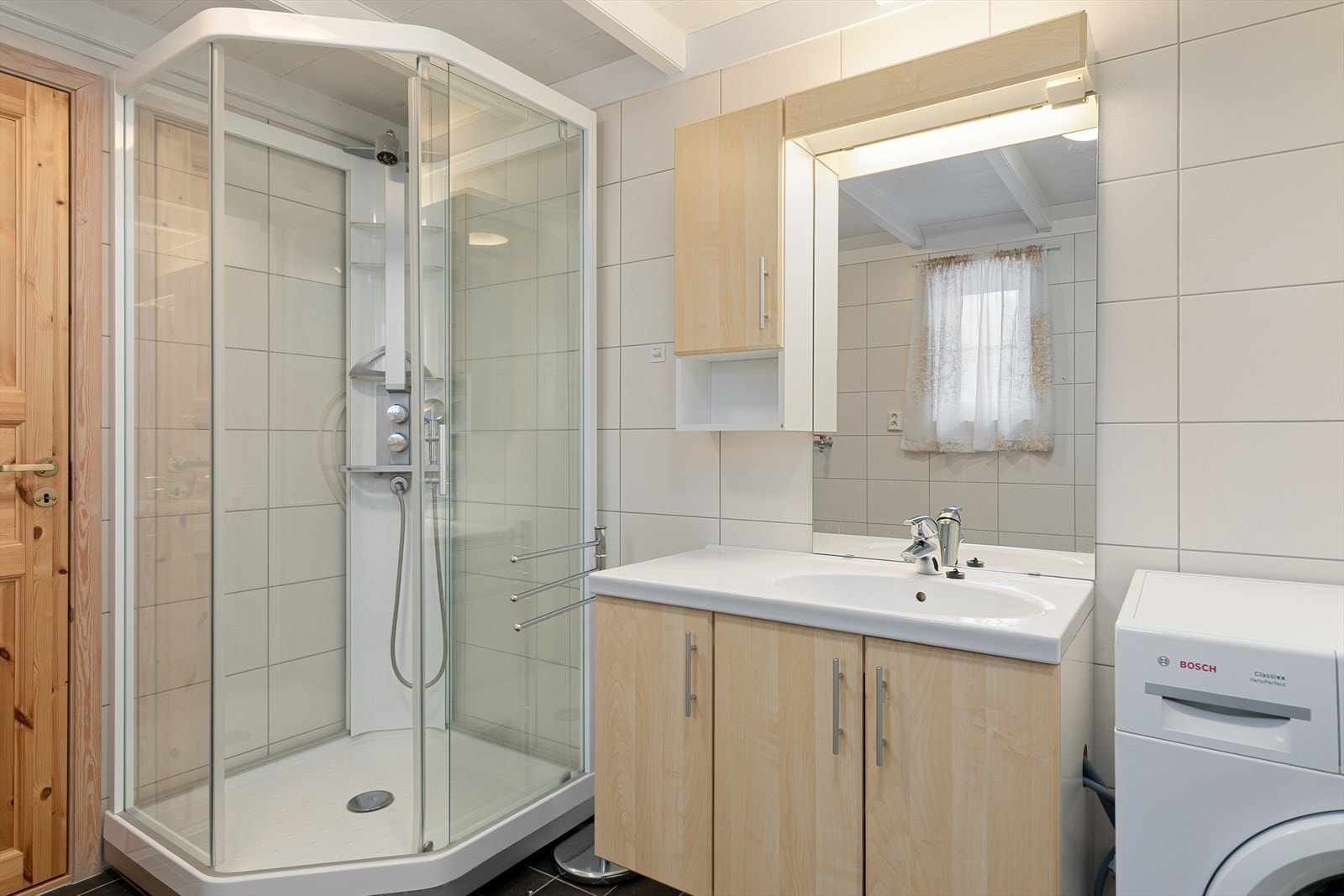 Badet har fliser på både golv og veggar, og er utstyrt med dusjhjørne, toalett og servant med innredning. Galleribilde