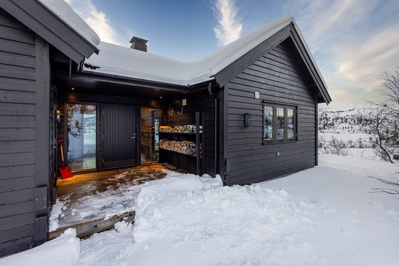 Pent og vedlikeholdt inngangsparti med inngang til vaskerom og praktisk løsning for stabling av ved Galleribilde