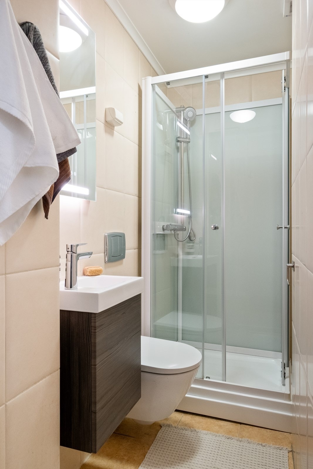 Flislagt bad med gulvvarme, dusjkabinett, servantskap og veggmontert toalett Galleribilde