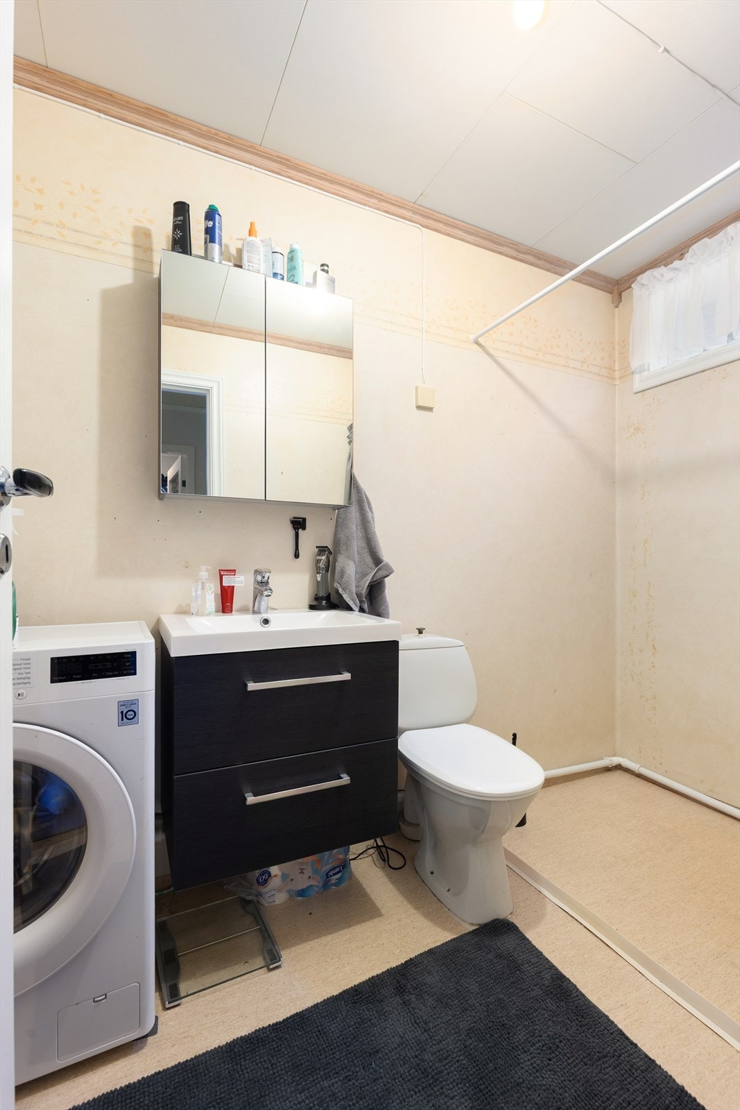 Badet har belegg på gulv med varmekabler, og innredning med skuffer og heldekkende servant. Badet er også innredet med speilskap, veggmontert dusj med forheng, toalett og opplegg for vaskemaskin. På veggoverflatene er det våtromstapet. Galleribilde