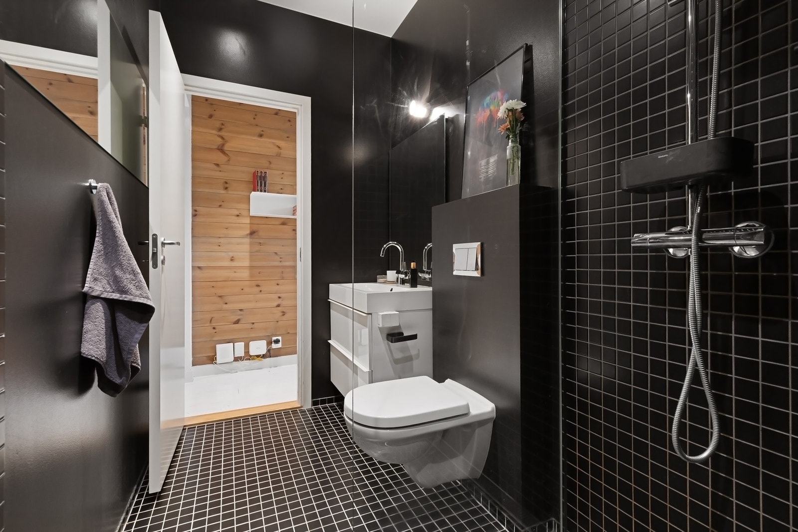 Mørke mosaikkfliser gir badet et stilrent preg. Badet er innredet med vegghengt servantskap, speil med belysning, vegghengt toalett og dusjhjørne med glassvegg samt regn- og hånddusj. Galleribilde