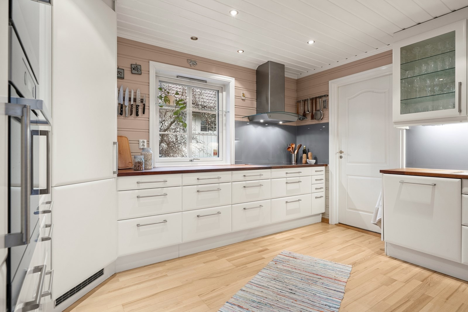 Kjøkkenet har en tidløs innredning med hvite, glatte fronter, heltre benkeplate med underlimt kum og nedfelt bred Miele-koketopp. Galleribilde