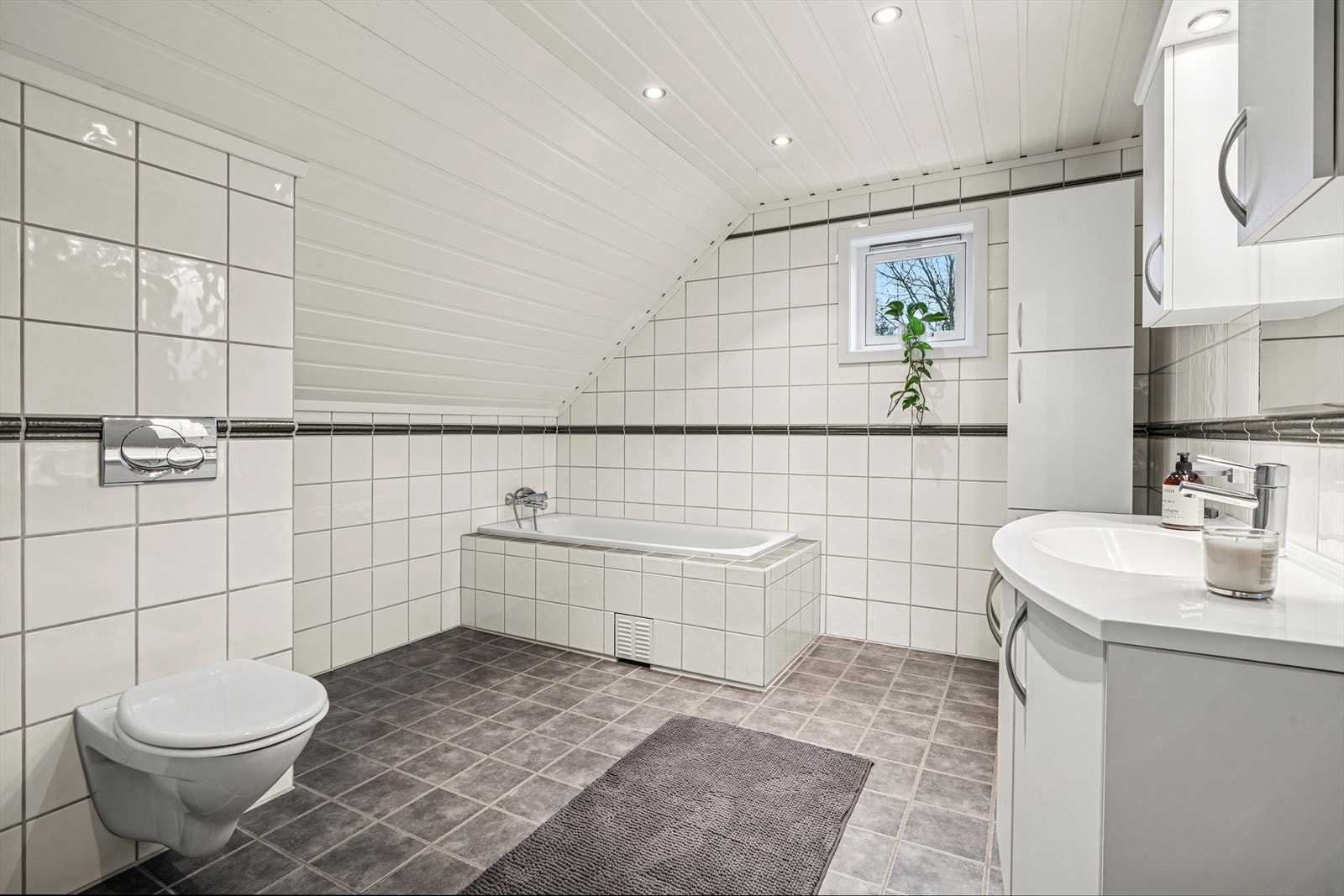 Innredningen består av baderomsinnredning med nedfelt servant, veggmontert toalett, dusjkabinett og innfliset badekar Galleribilde