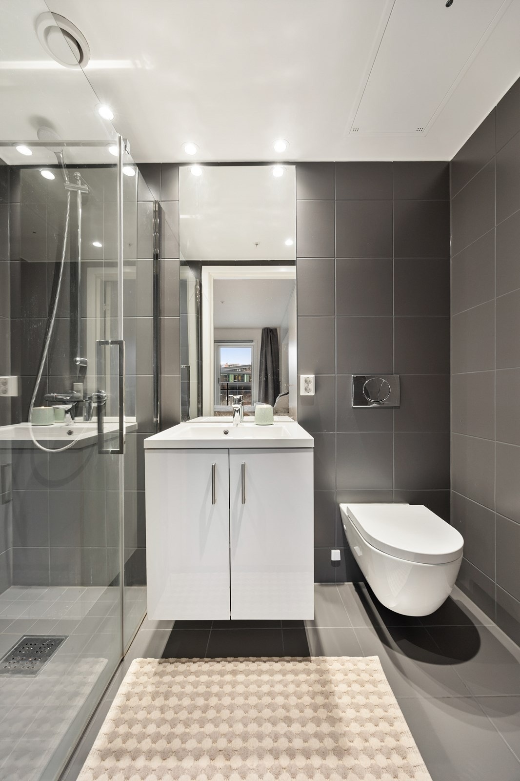 Badet er utstyrt med vegghengt toalett, servantinnredning og dusj med glassdører. Galleribilde