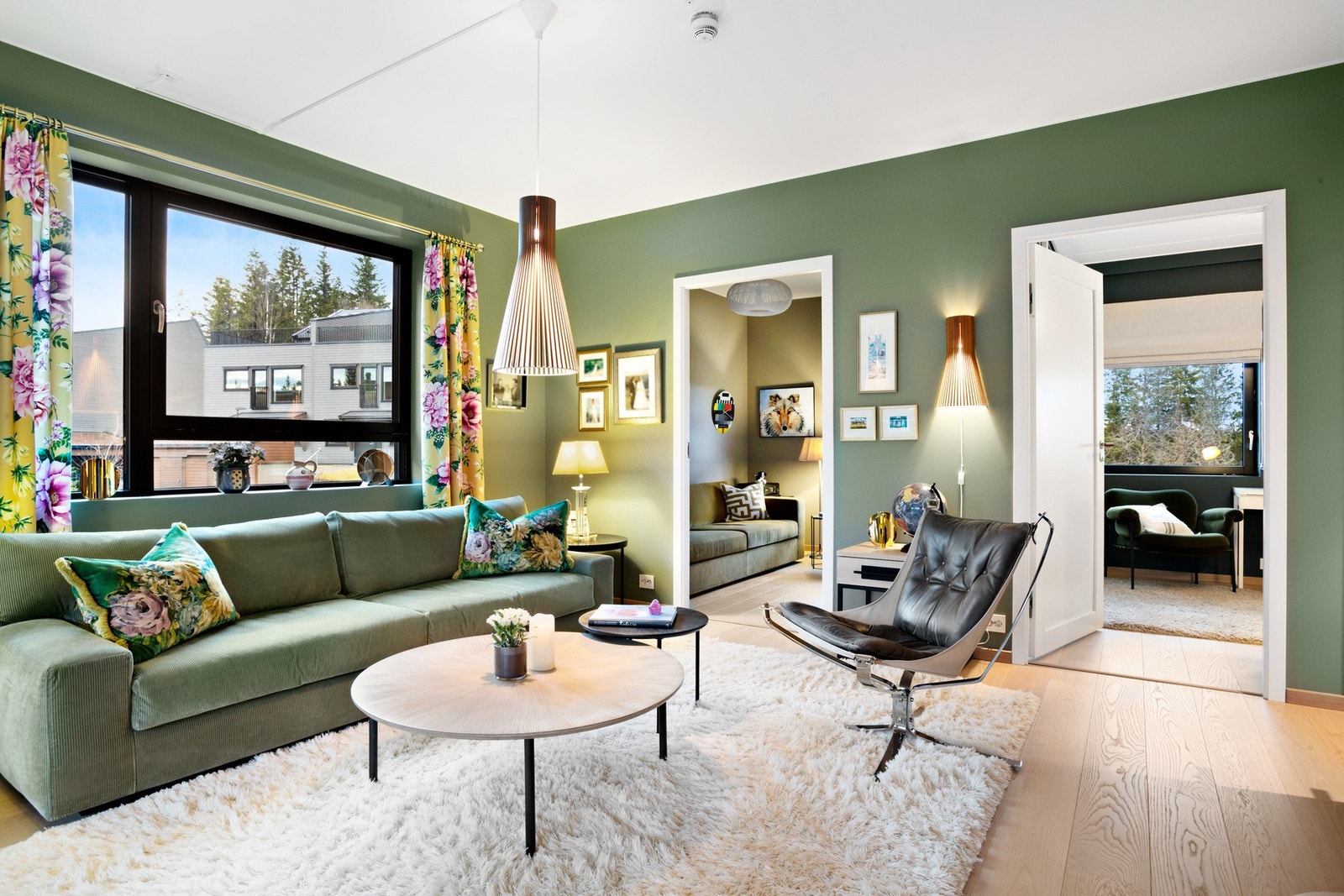 Lyst og stilfull stue med grønne vegger, fargerike tekstiler og moderne belysning, kombinert med både spiseplass og romslig sofakrok. Galleribilde