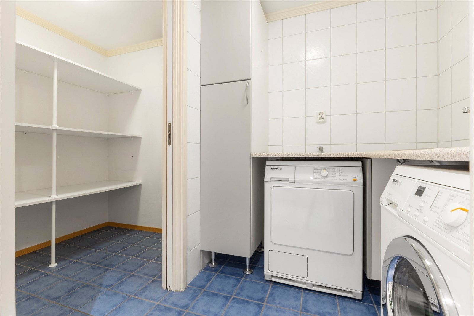 En praktisk skyvedør fører videre inn til vaskerommet, hvor det er opplegg for både vaskemaskin og tørketrommel. Rommet er utstyrt med høyskap, benkeplate og utslagsvask. Fra vaskerommet er det inngang til en romslig bod med gode oppbevaringsmuligheter. Galleribilde