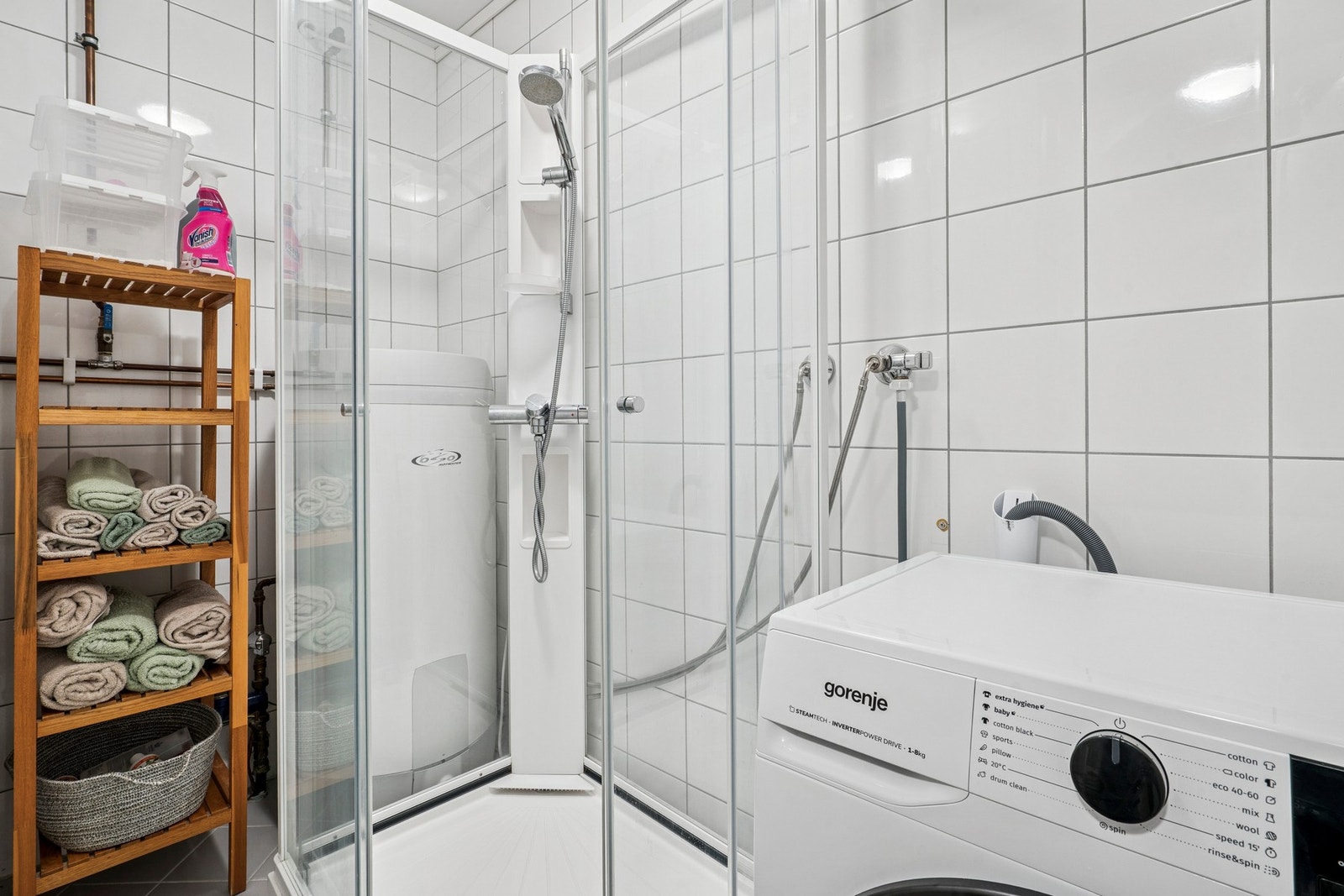 Et romslig vaskerom med flislagt gulv og dusjkabinett samt opplegg for vaskemaskin og tørketrommel. Galleribilde