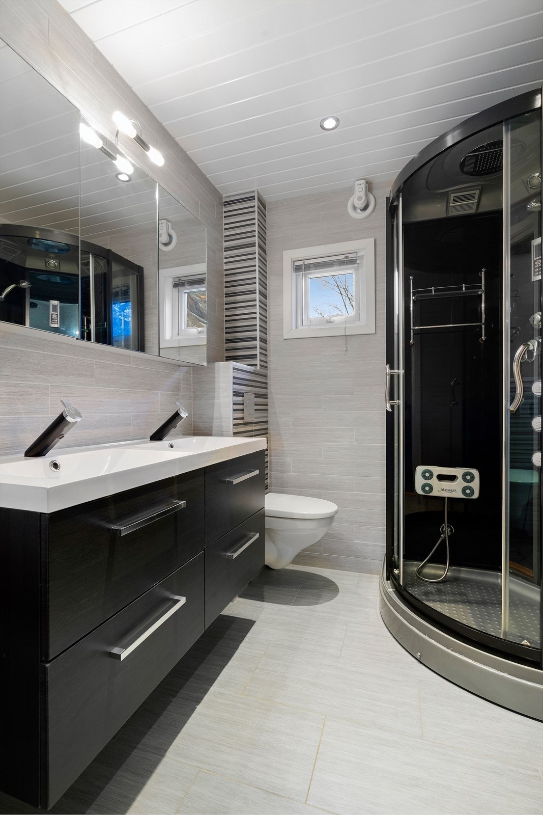 Flislagt bad utstyrt med vegghengt wc, dusjkabinett og heldekkende dobbelservant med under- og speilskap. Galleribilde