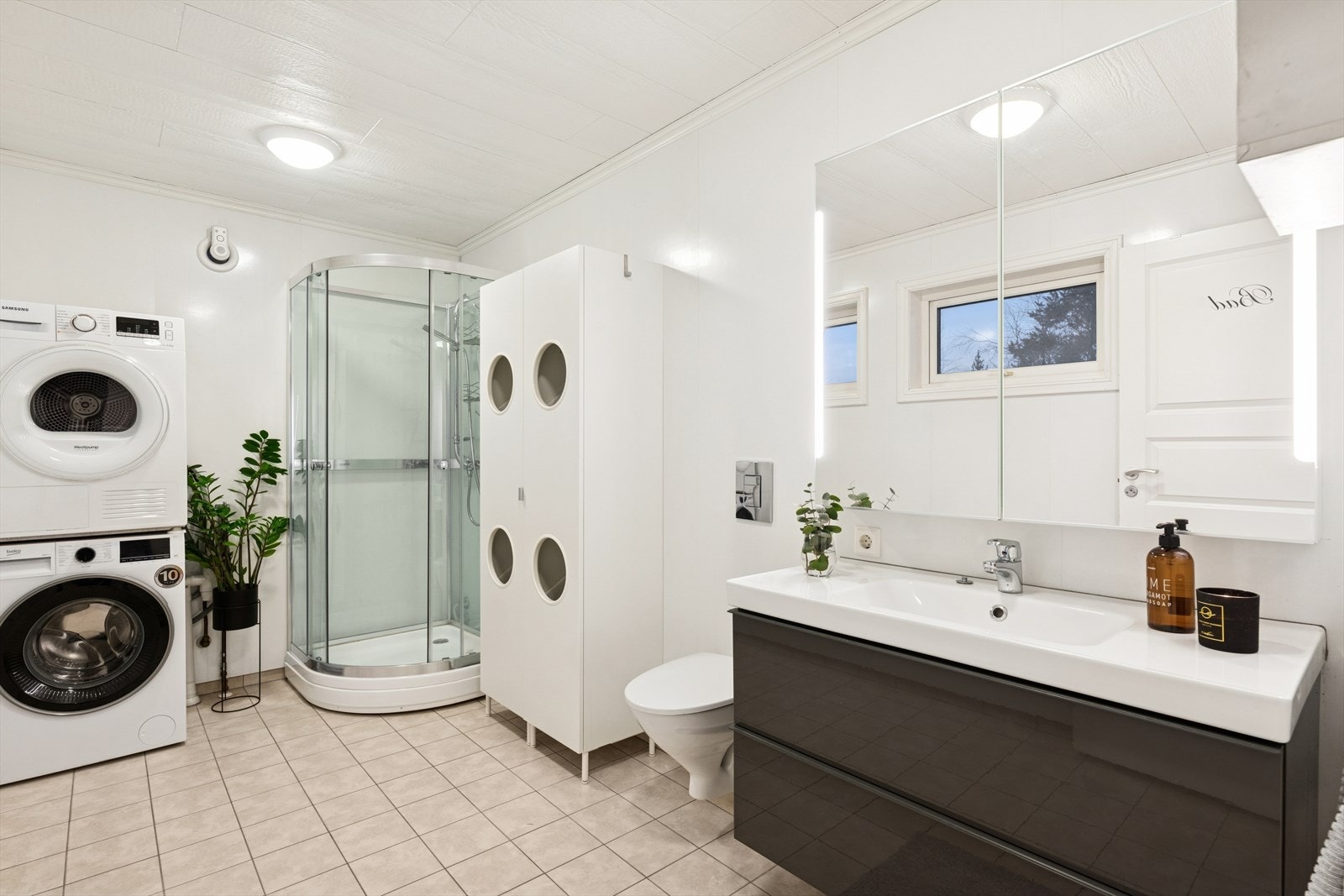 Rommet er innredet med en servantinnredning med nedfelt servant, veggmontert toalett, dusjkabinett og det er opplegg for vaskemaskin. Blandebatteri ble skiftet på badet i 1. etasje og på kjøkken i 2025. Baderomsinnredning ble byttet i 2018. Galleribilde