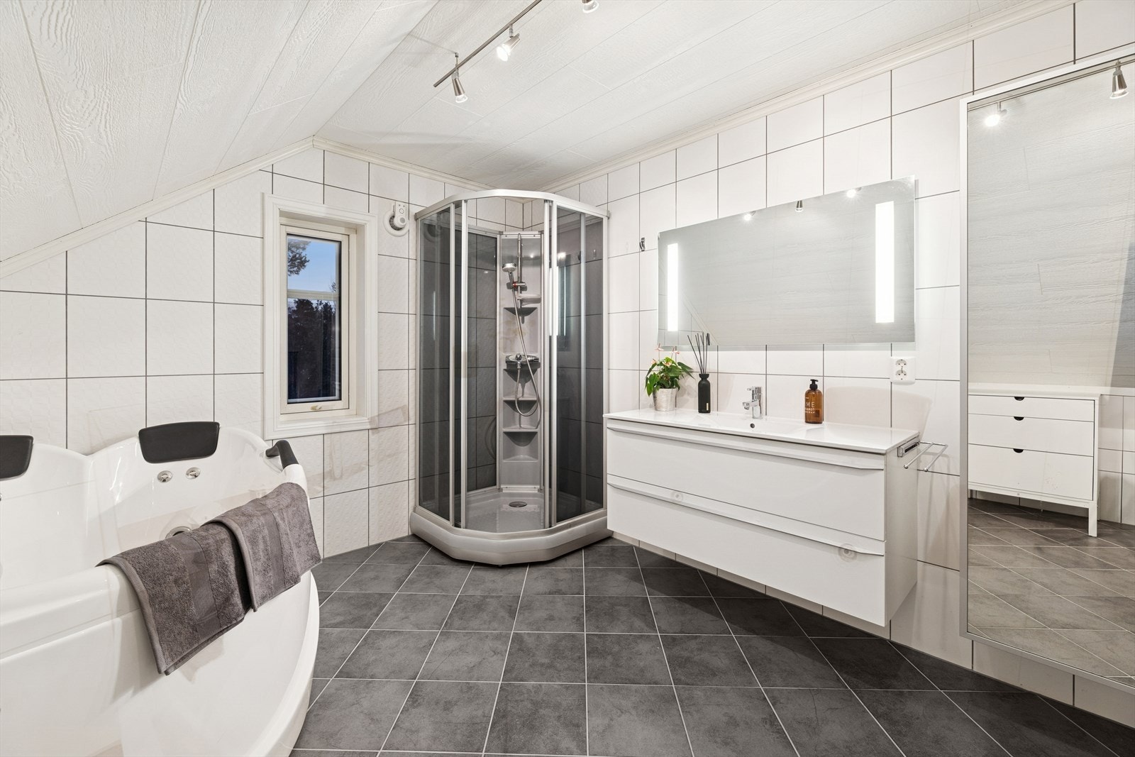 Innredningen inkluderer en servantinnredning med nedfelt servant, et veggmontert toalett, dusjkabinett og et badekar. Galleribilde