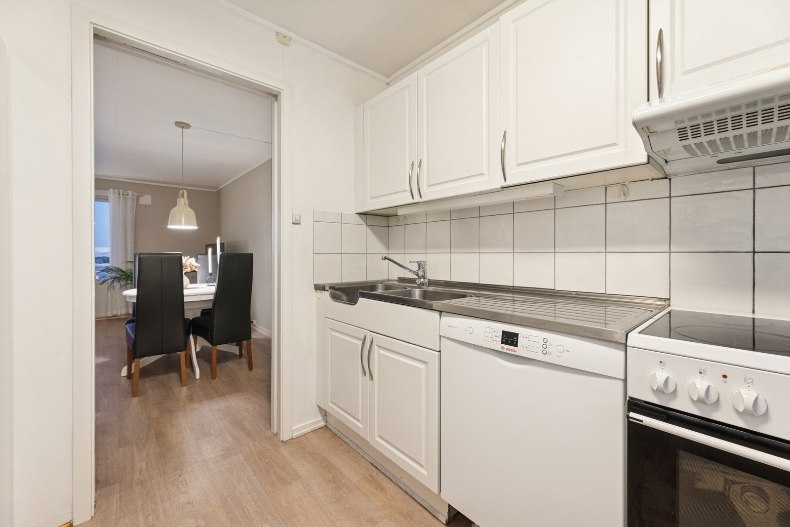 Kjøkkenet har en innredning med profilerte fronter, benkeplate i laminat og fliser over deler av benk. Galleribilde