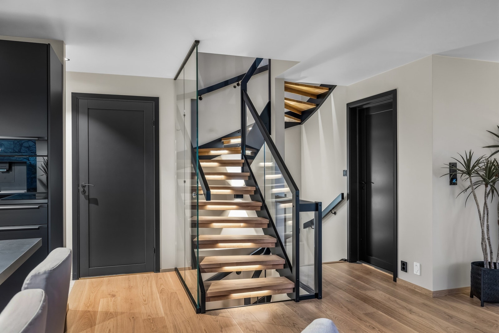 Stilfull trappeoppgang med hvitlaserte trinn i hardved og rekkverk i glass og stål, et stilrent blikkfang som binder etasjene elegant sammen Galleribilde