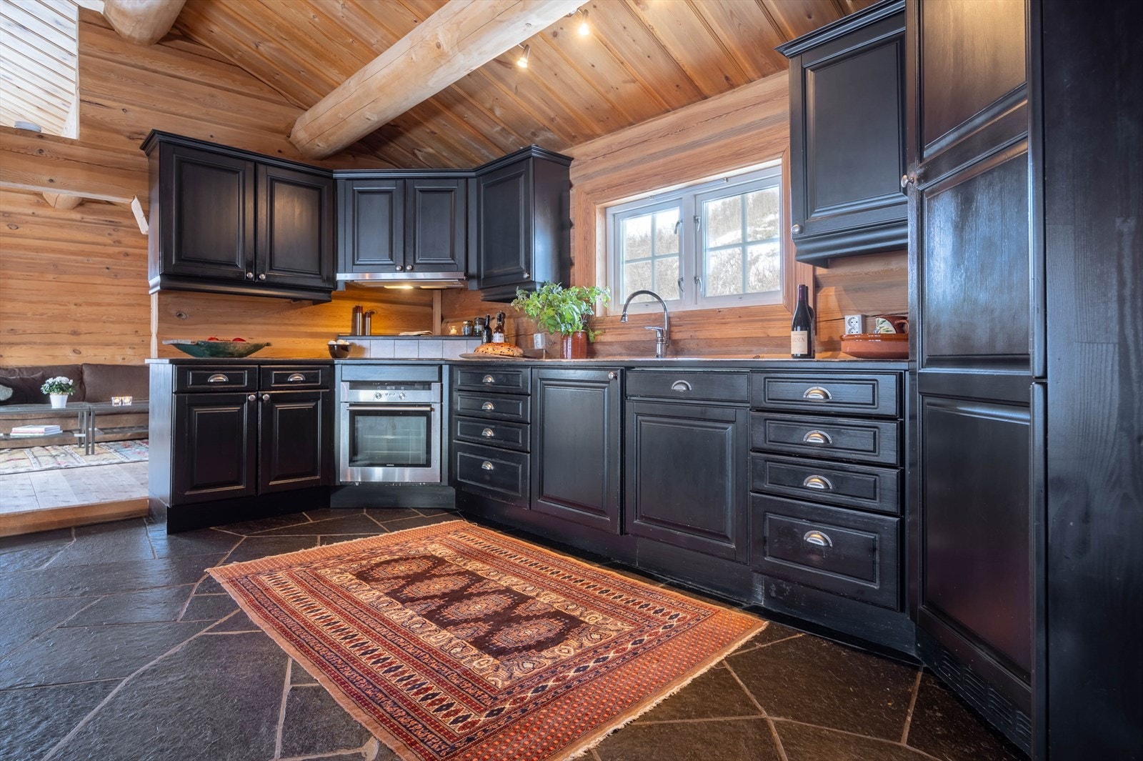 Et tidsriktig kjøkken i mørke toner, der flisbelagt benkeplate og integrerte hvitevarer smelter sømløst inn i tømmerets varme. Galleribilde