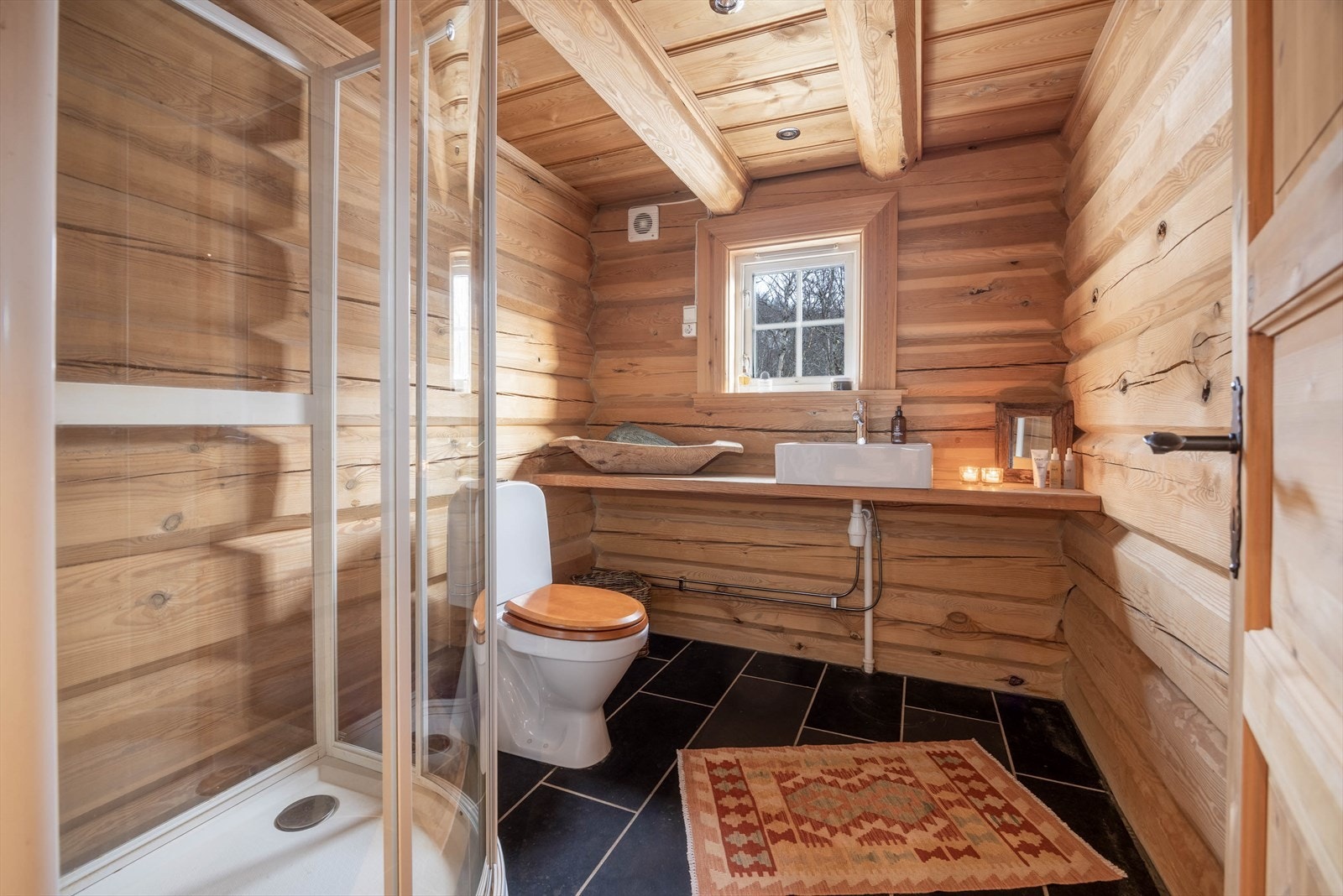 Et stemningsfullt bad der fliser møter tømmer - en harmonisk kombinasjon av komfort og hyttekos. Galleribilde