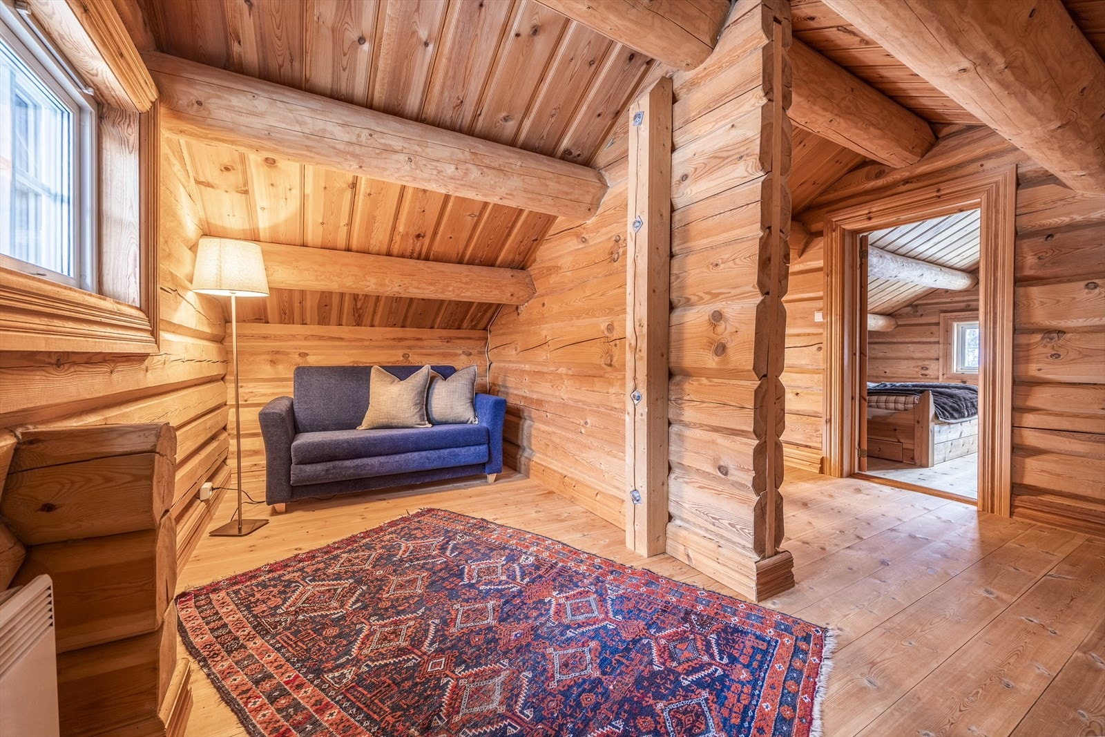 Loftsstuen inviterer til ro og hyttekos, med varme tømmervegger og myke kroker for avslapning. Galleribilde