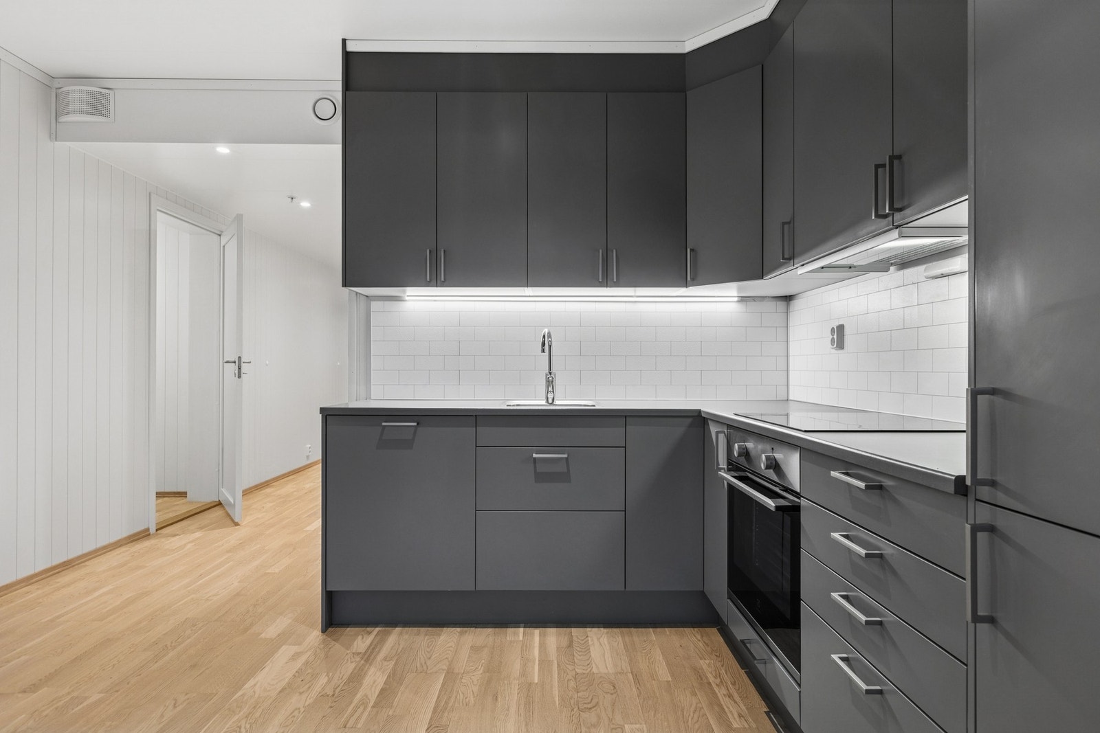 Pent og funksjonelt kjøkken med gode arbeidsflater og rikelig med oppbevaringsmuligheter. Innredningen har et moderne uttrykk, med profilerte fronter, integrerte hvitevarer og benkeplater i laminat som sørger for enkelt renhold. Galleribilde