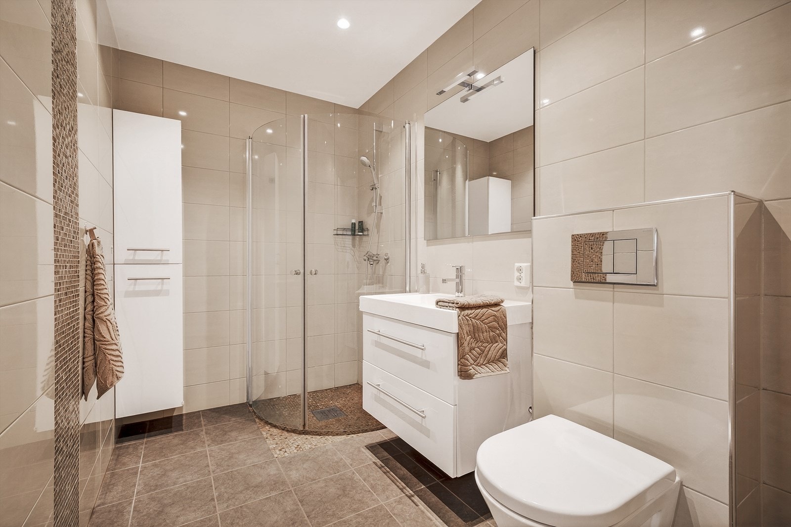 Moderne bad med dusjkabinett, stilrene fliser og elegant servant. Lyse farger gir et innbydende og romslig inntrykk. Galleribilde