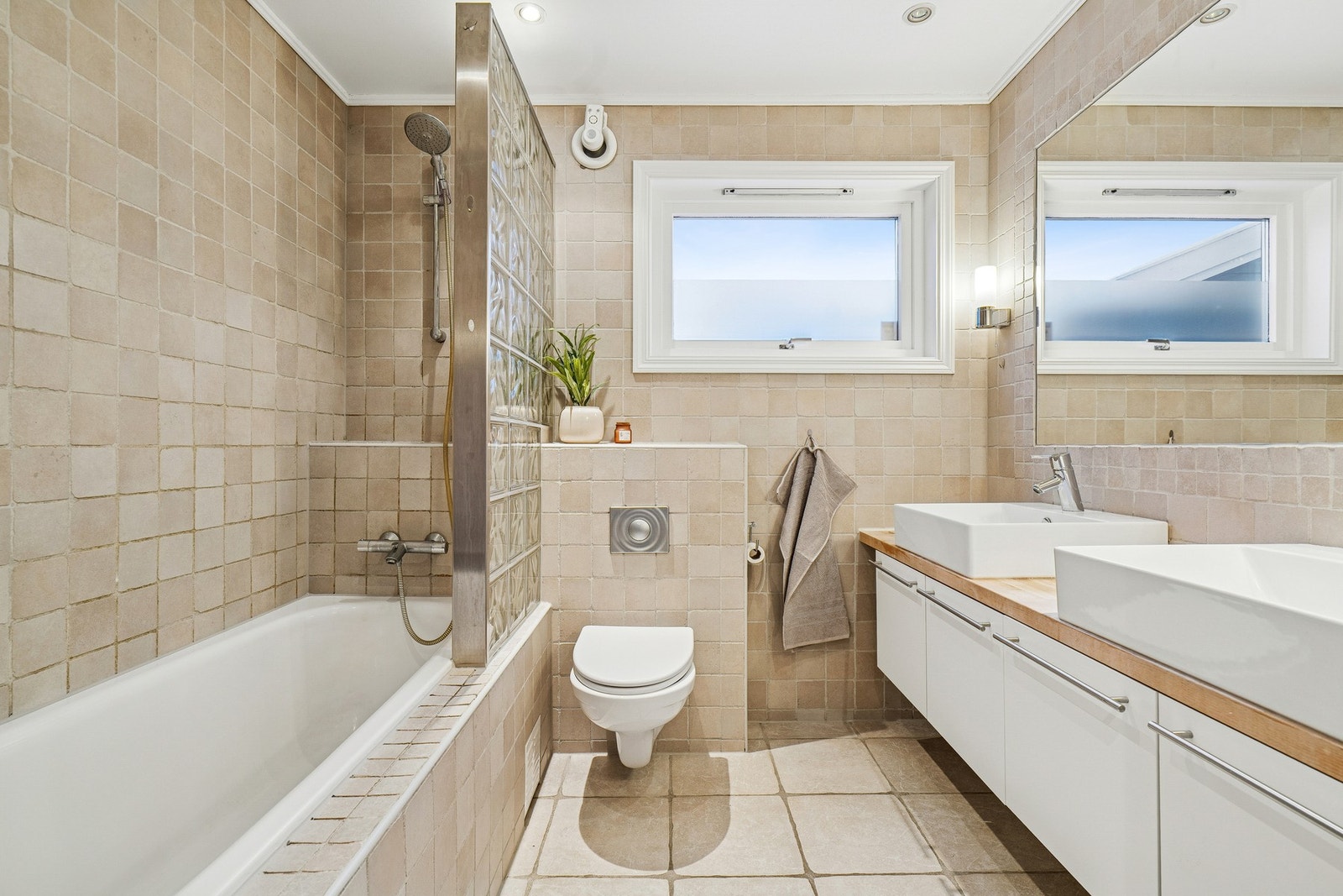 Flislagt bad innredet med to servanter, badekar og vegghengt WC. Varmekabler i gulv. Galleribilde