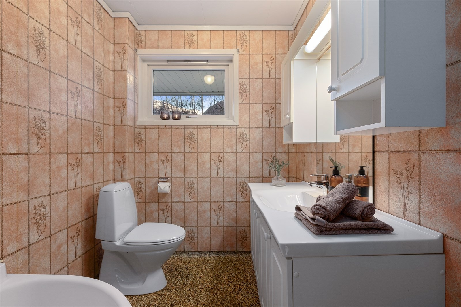 Eldre bad utstyrt med dusjhjørne, toalett og servant med innredning. Galleribilde